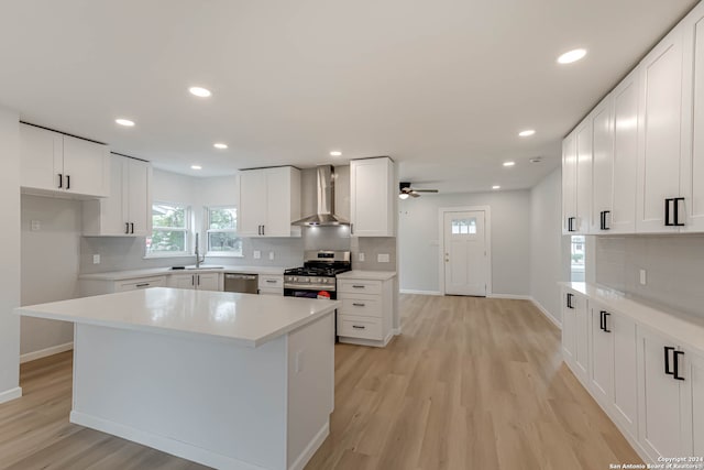 kitchen featuring wall chimney range hood, white cabinetry, light hardwood / wood-style flooring, and appliances with stainless steel finishes