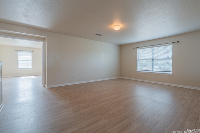 empty room featuring a wealth of natural light, a textured ceiling, and light hardwood / wood-style flooring