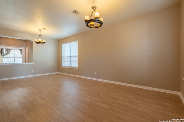 empty room with a wealth of natural light, wood-type flooring, and an inviting chandelier