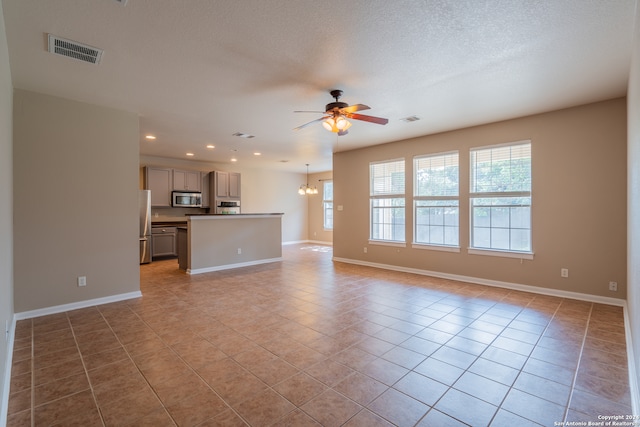 unfurnished living room with a textured ceiling, ceiling fan with notable chandelier, and light tile patterned floors