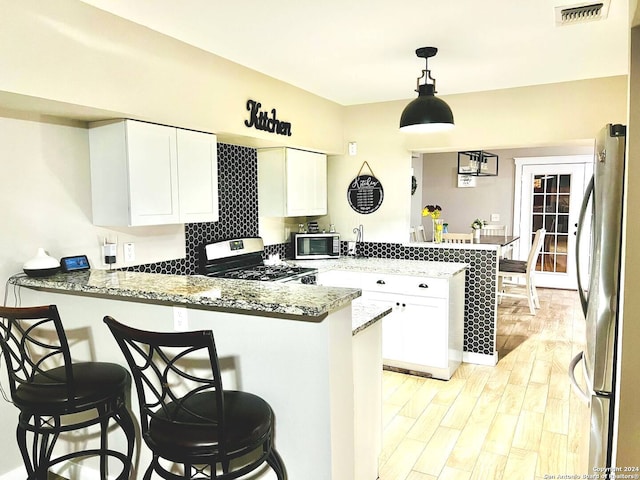 kitchen with white cabinets, kitchen peninsula, stainless steel appliances, and light hardwood / wood-style floors