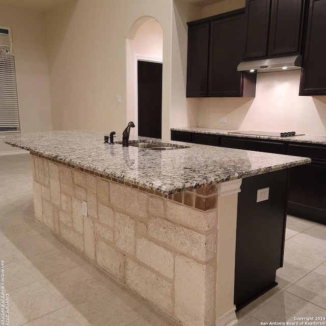 kitchen featuring sink, a kitchen island with sink, light stone counters, and black electric cooktop