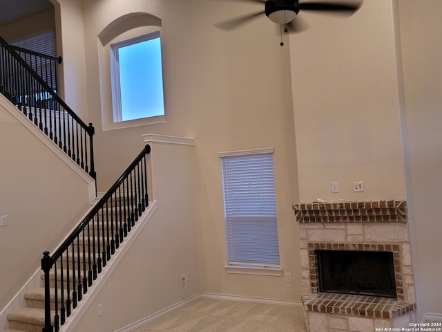 stairs featuring a high ceiling, a fireplace, ceiling fan, and carpet flooring