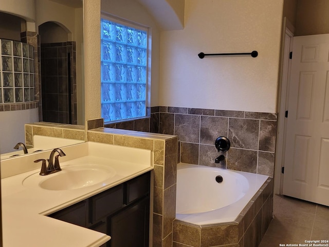 bathroom with tile patterned flooring, tiled tub, and vanity