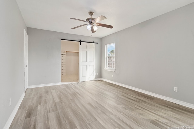 unfurnished bedroom with a spacious closet, a closet, ceiling fan, light hardwood / wood-style flooring, and a barn door