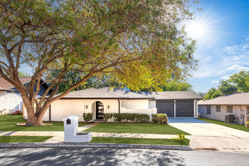 ranch-style house featuring a garage, cooling unit, and a front yard