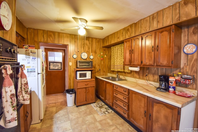 kitchen with wooden walls, white appliances, sink, and ceiling fan