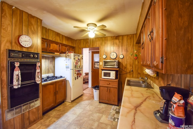 kitchen with wooden walls, sink, white appliances, and ceiling fan