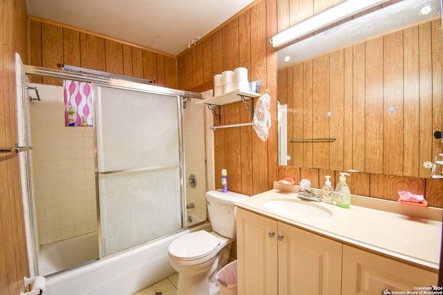 full bathroom with wood walls, vanity, bath / shower combo with glass door, tile patterned floors, and toilet