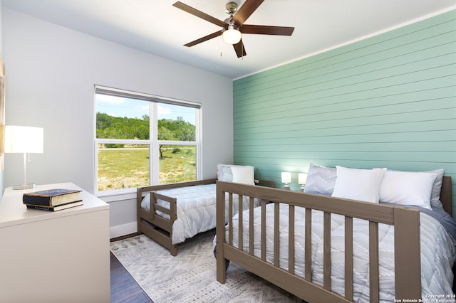 bedroom featuring wood-type flooring, ceiling fan, and wooden walls