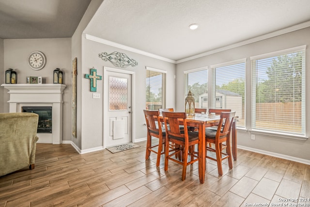 dining room featuring ornamental molding, light hardwood / wood-style flooring, a textured ceiling, and vaulted ceiling