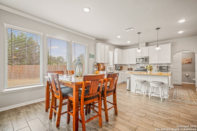 dining room with a textured ceiling, sink, light wood-type flooring, and ornamental molding