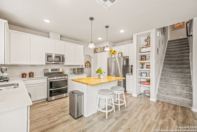 kitchen featuring white cabinets, light hardwood / wood-style flooring, a kitchen island, backsplash, and appliances with stainless steel finishes