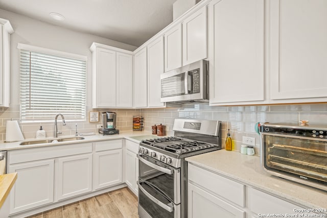 kitchen featuring stainless steel appliances, sink, tasteful backsplash, light hardwood / wood-style flooring, and white cabinets