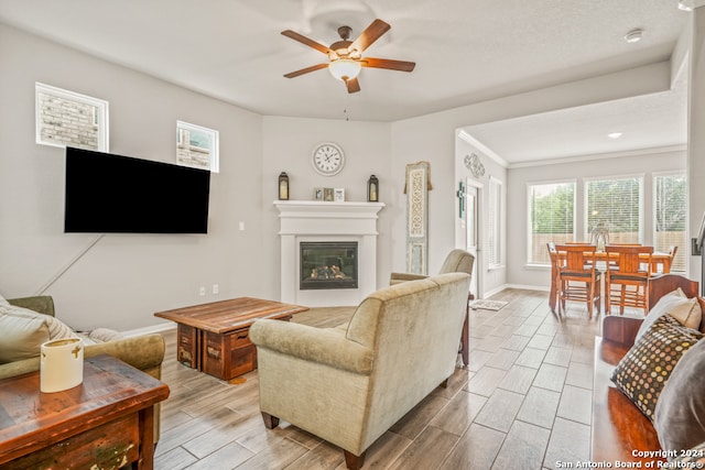 living room featuring light hardwood / wood-style floors, ceiling fan, a textured ceiling, and ornamental molding