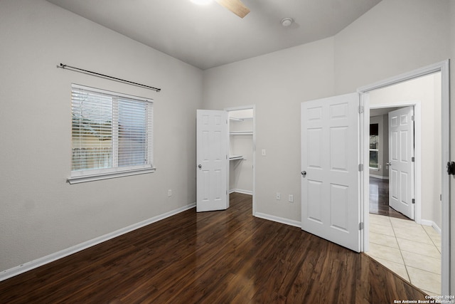 unfurnished bedroom with ceiling fan, a walk in closet, a closet, and dark hardwood / wood-style flooring