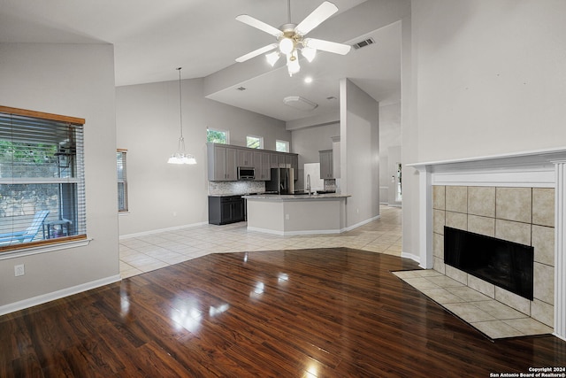 unfurnished living room featuring light hardwood / wood-style floors, sink, a tiled fireplace, high vaulted ceiling, and ceiling fan with notable chandelier