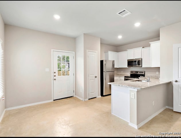 kitchen with light stone counters, white cabinetry, appliances with stainless steel finishes, sink, and kitchen peninsula