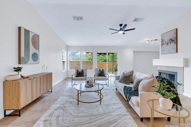 living room with a tile fireplace, vaulted ceiling, and ceiling fan