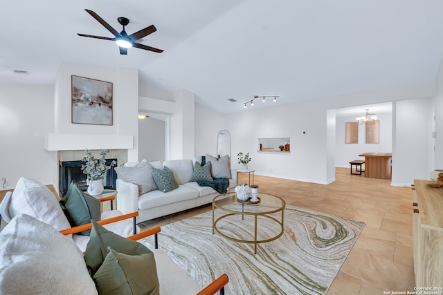 living room with a tiled fireplace, ceiling fan with notable chandelier, rail lighting, and vaulted ceiling