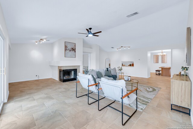 living room with a tile fireplace, ceiling fan with notable chandelier, and vaulted ceiling