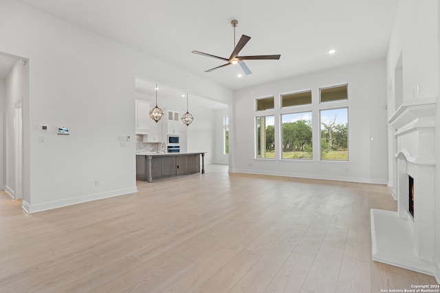 unfurnished living room with ceiling fan with notable chandelier and light hardwood / wood-style flooring