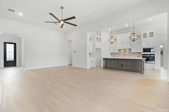 unfurnished living room with ceiling fan with notable chandelier, a healthy amount of sunlight, and light hardwood / wood-style flooring