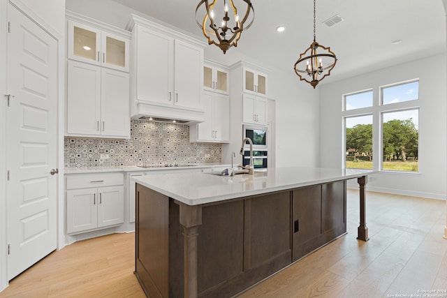 kitchen with white cabinets, a chandelier, an island with sink, and decorative light fixtures