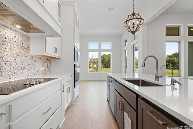 kitchen with black electric cooktop, decorative backsplash, light stone countertops, white cabinetry, and premium range hood