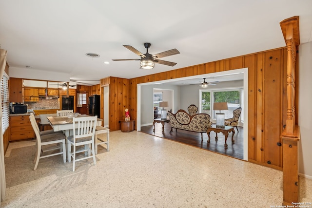 dining room featuring ceiling fan and wooden walls