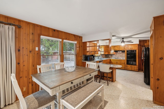 dining space featuring wooden walls, sink, and ceiling fan