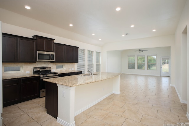 kitchen featuring tasteful backsplash, appliances with stainless steel finishes, light stone countertops, ceiling fan, and a kitchen island with sink