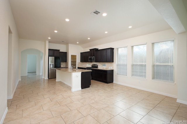 kitchen with a center island with sink, light stone counters, tasteful backsplash, light tile patterned flooring, and appliances with stainless steel finishes