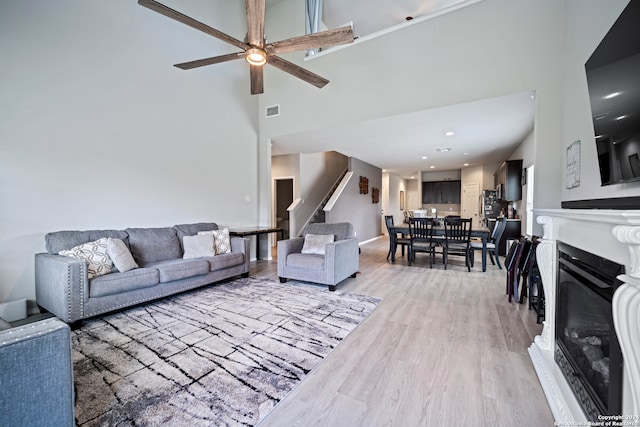 living room featuring light wood-type flooring, ceiling fan, and a towering ceiling