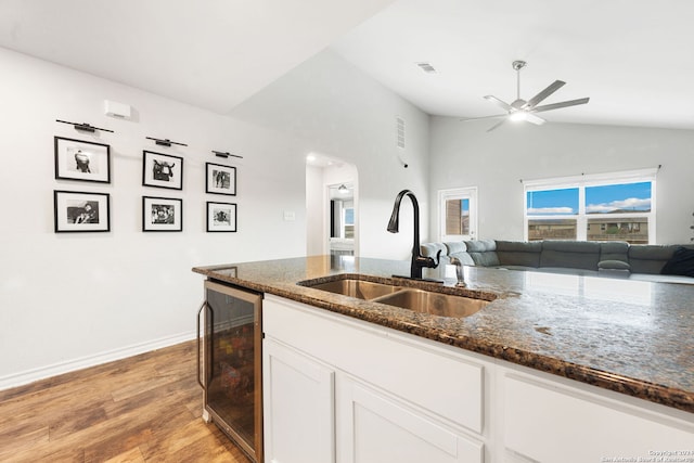 kitchen featuring lofted ceiling, dark stone counters, white cabinets, sink, and wine cooler