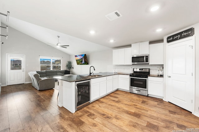 kitchen with light wood-type flooring, appliances with stainless steel finishes, vaulted ceiling, beverage cooler, and kitchen peninsula