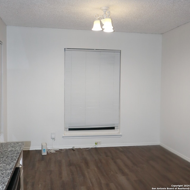 empty room with an inviting chandelier, a textured ceiling, and dark hardwood / wood-style floors