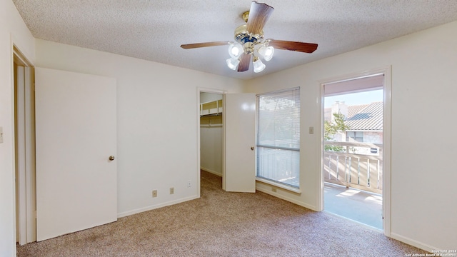 unfurnished bedroom with light colored carpet, a textured ceiling, ceiling fan, a closet, and a walk in closet