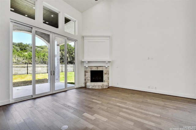 228 Dulce, Boerne, TX 78006 - unfurnished living room featuring a towering ceiling, wood finished floors, baseboards, and a stone fireplace