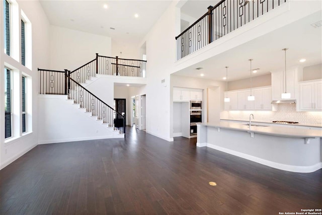 228 Dulce, Boerne, TX 78006 - unfurnished living room featuring a towering ceiling, healthy amount of natural light, a sink, dark wood-style floors, and stairway
