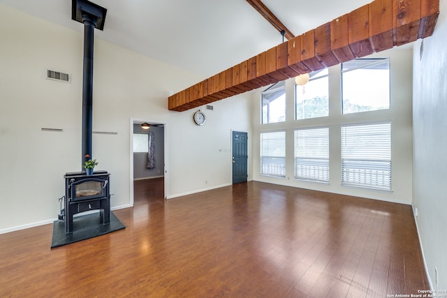 unfurnished living room with dark wood-type flooring, beam ceiling, a wood stove, and high vaulted ceiling