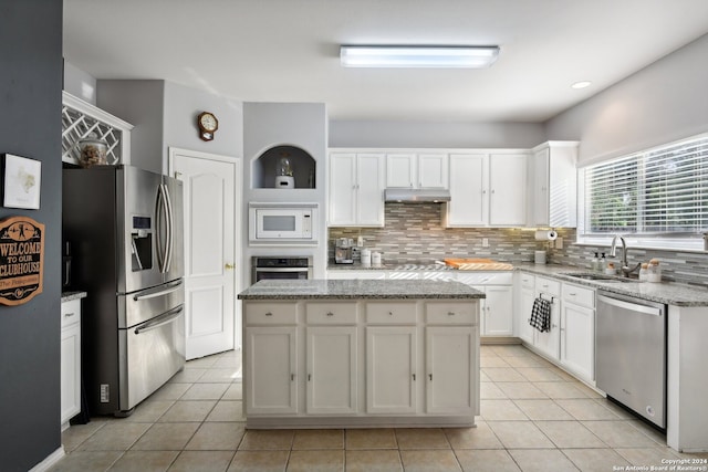 kitchen with white cabinets, sink, light stone countertops, a kitchen island, and stainless steel appliances