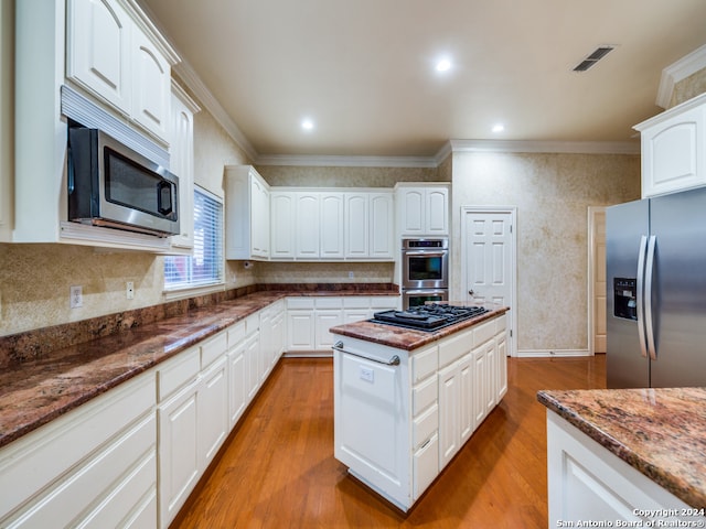 kitchen featuring wood-type flooring, ornamental molding, dark stone counters, appliances with stainless steel finishes, and white cabinets