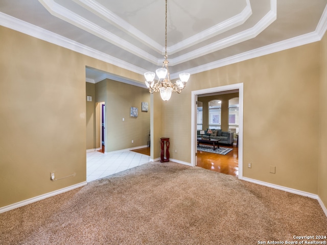 carpeted empty room with a notable chandelier, a tray ceiling, and ornamental molding