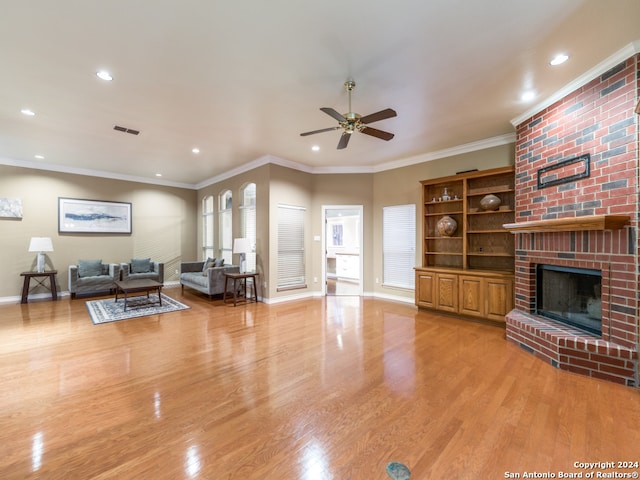 living room featuring a fireplace, ceiling fan, light wood-type flooring, and crown molding