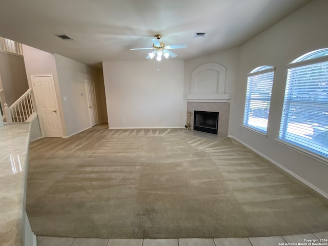 unfurnished living room with a tile fireplace, light colored carpet, and ceiling fan