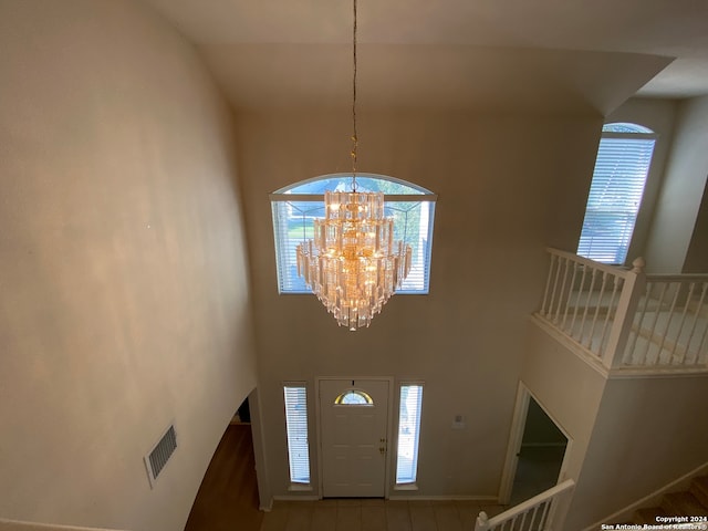 foyer with a wealth of natural light, a chandelier, wood-type flooring, and a towering ceiling