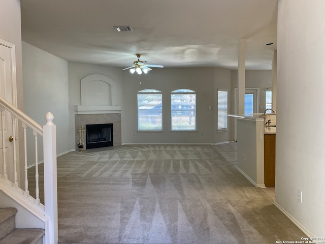 unfurnished living room with light carpet, ceiling fan, and a tile fireplace