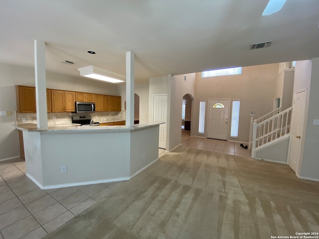 kitchen featuring stainless steel appliances, light colored carpet, kitchen peninsula, and tasteful backsplash