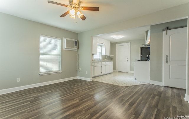 unfurnished living room with sink, a wall unit AC, dark hardwood / wood-style floors, ceiling fan, and a barn door